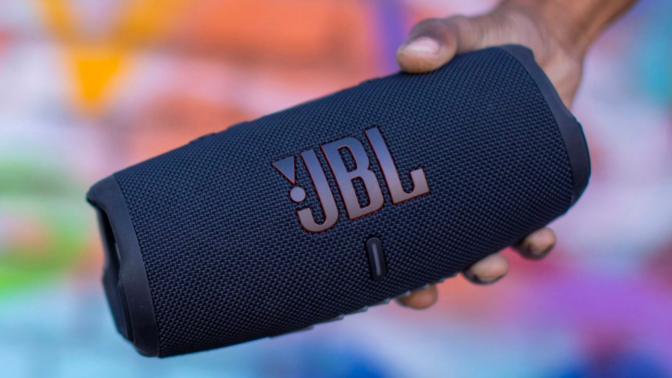 a close-up of a person holding a jbl charge 5 in front of a colorful wall