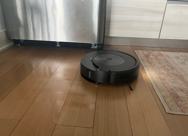 Roomba cleaning hardwood floor with refrigerator and rug in background